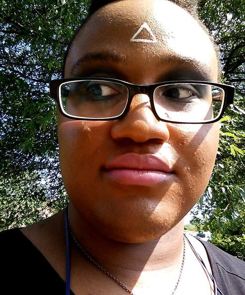 A picture of myself, a black person, wearing smeared dark make up and looking off to the side with trees in the background.