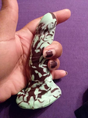 Image is a smaller dildo in the palm of my hand. It has an oval base and looks vaguely phallic with swirls of brown & mint green to create a confectionery effect.