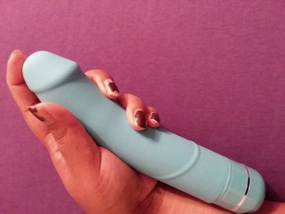 Image is a pale blue phallic vibrator against a purple background. I am holding the vibrator against my arm for a rough size referral, and it stretches from my palm to the middle of my arm.